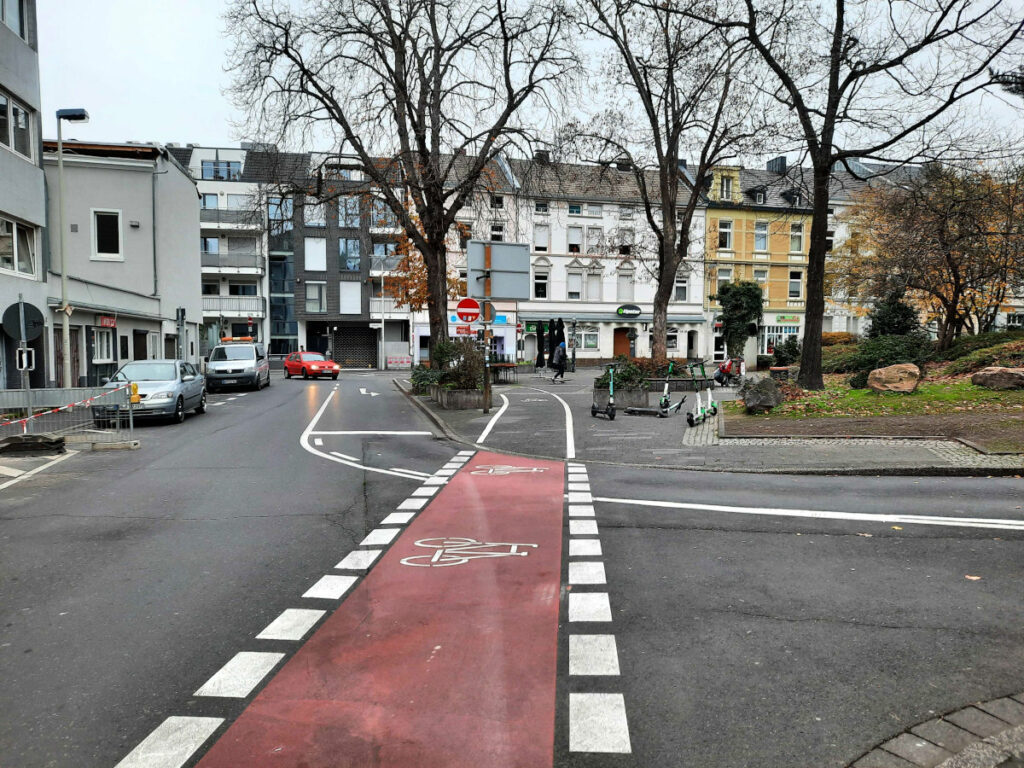 Ein Radweg führt von der Straße weg auf einen angrenzenden Platz um von dort wieder auf die Straße zu führen