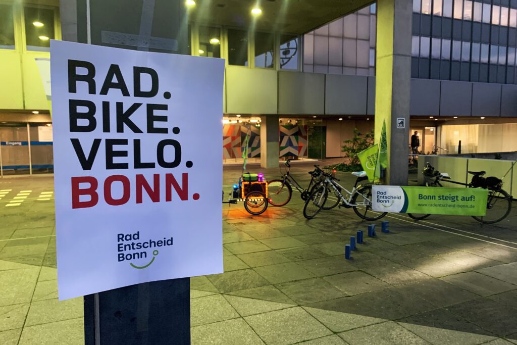 Ein Schild hängt vor dem Bonner Stadthaus. Darauf steht: Rad. Bike. Velo. Bonn