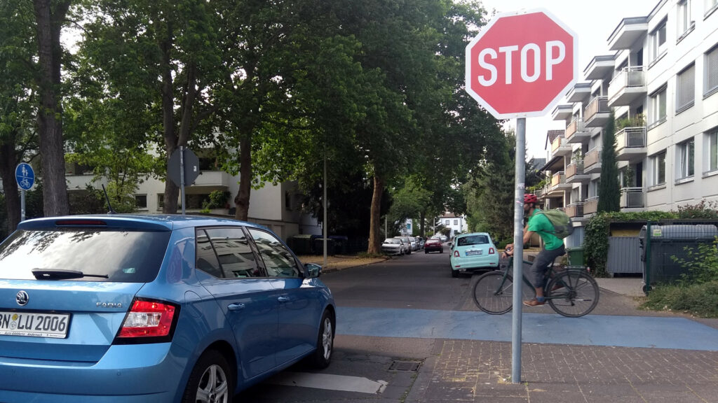 Ein blaues Auto hält an einem Stopp-Schild während der querende Radverkehr Vorfahrt hat