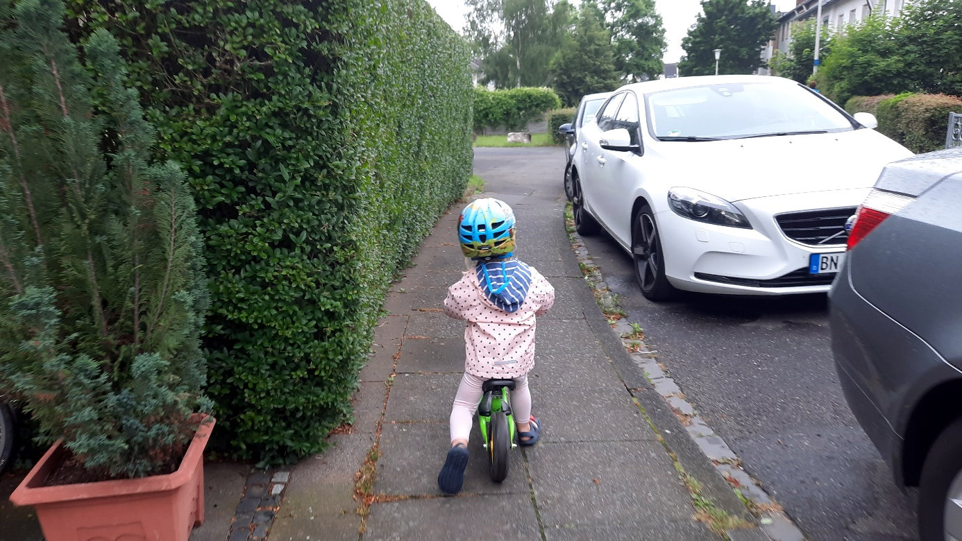 Ein Kind fährt mit seinem Laufrad auf einem Gehweg